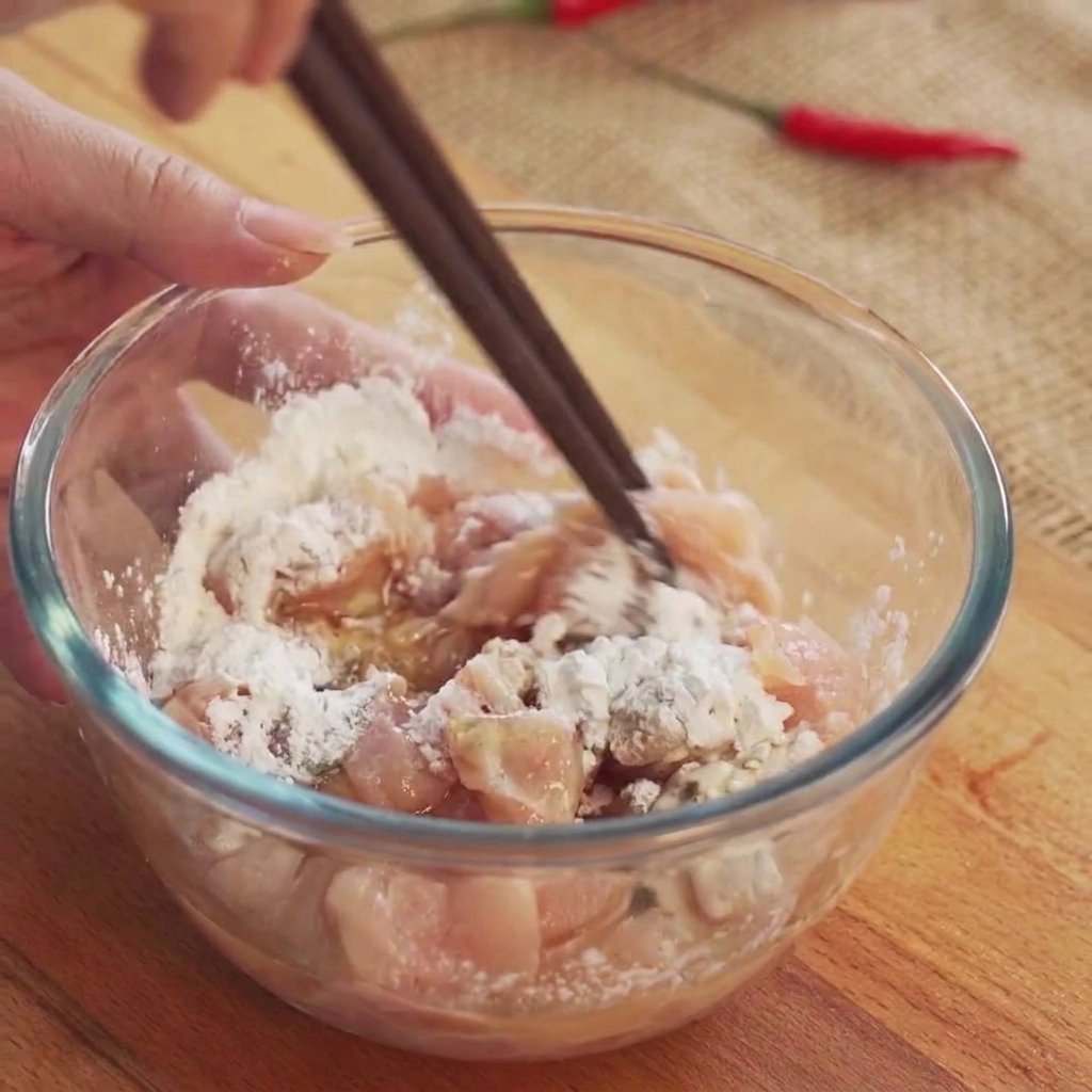 Hähnchenwürfel werden mit Stäbchen in einer transparenten Glasschüssel umgerührt, um die Marinade zu verteilen.