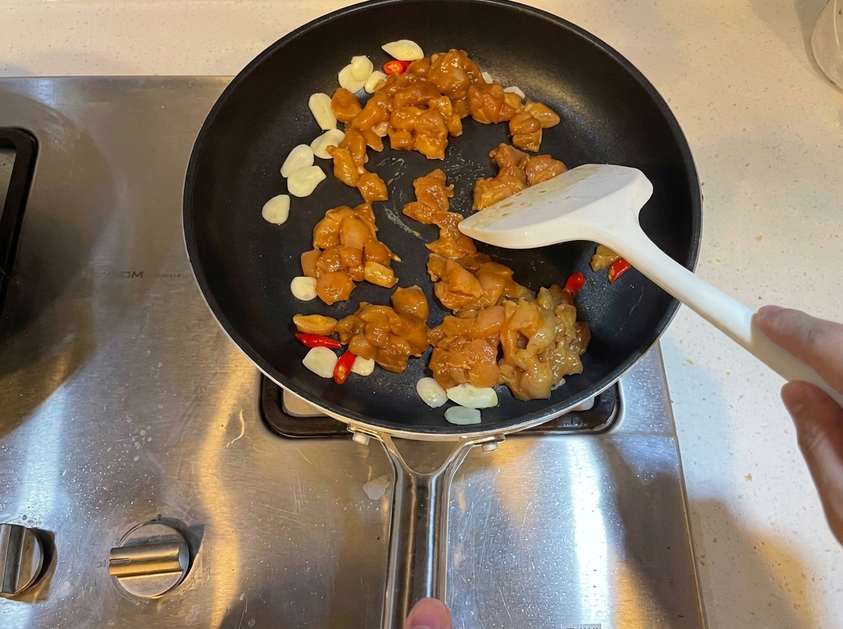 Marinierte Hähnchenwürfel werden in einer Pfanne mit Knoblauch und Chilis pfannengerührt.