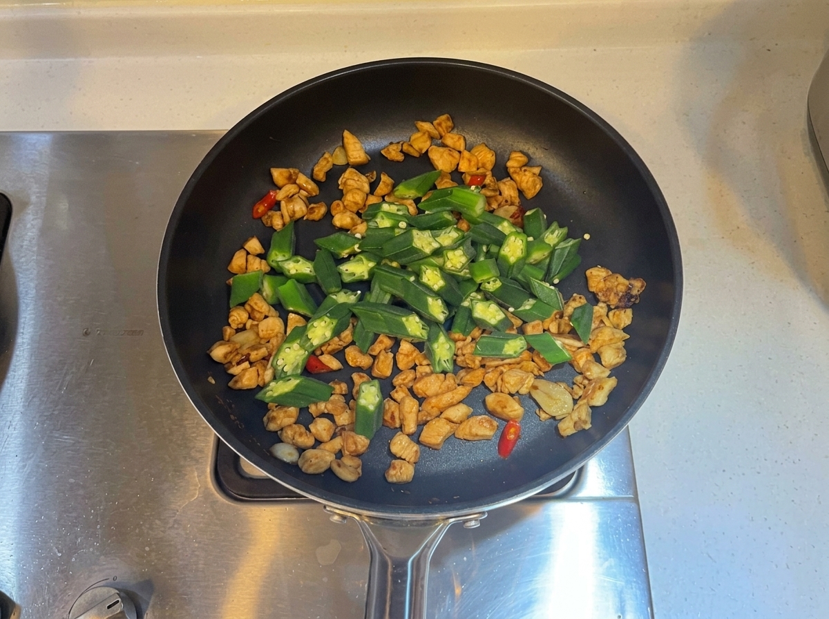 Grüne Okrascheiben in die Pfanne mit dem gekochten Hähnchen und den Aromaten gemischt.