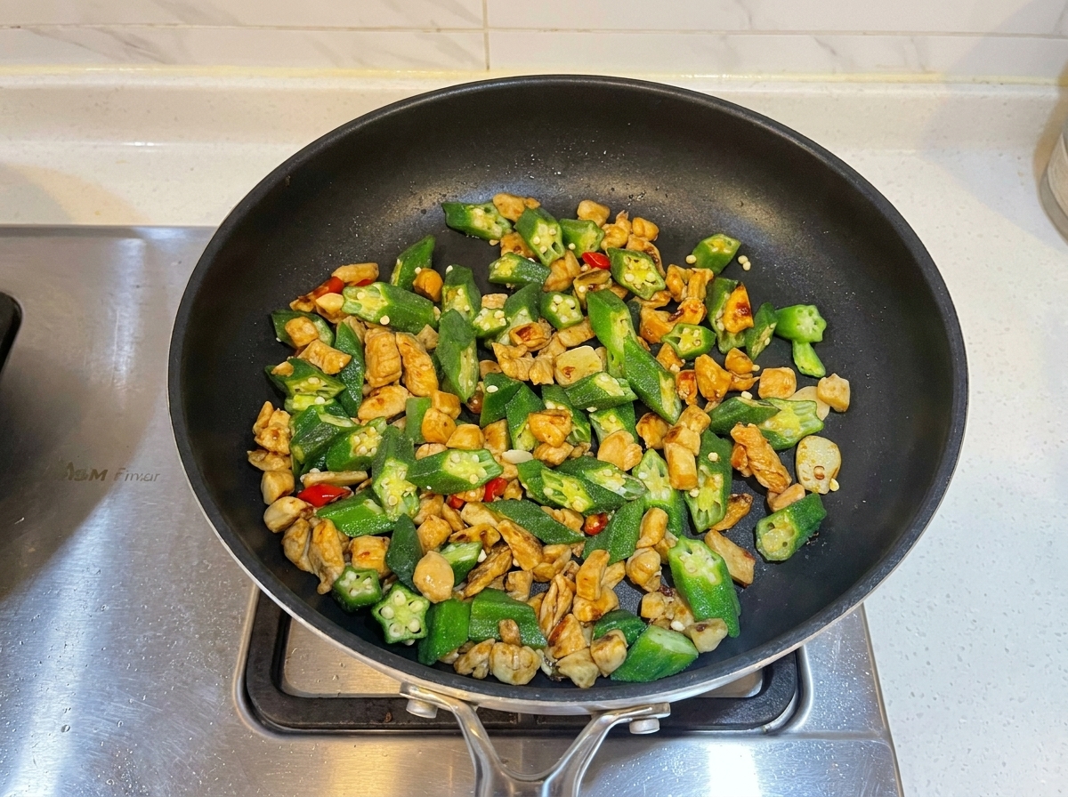 Austernsauce wird in der Pfanne zur Hähnchen-Okra-Mischung gegeben.
