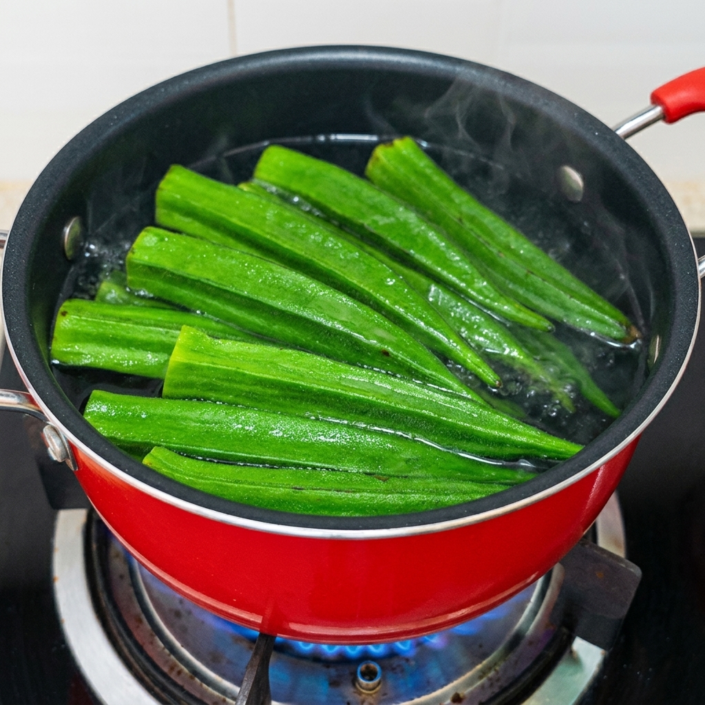 Grüne Okraschoten kochen in einem roten Topf in gewürztem Wasser.