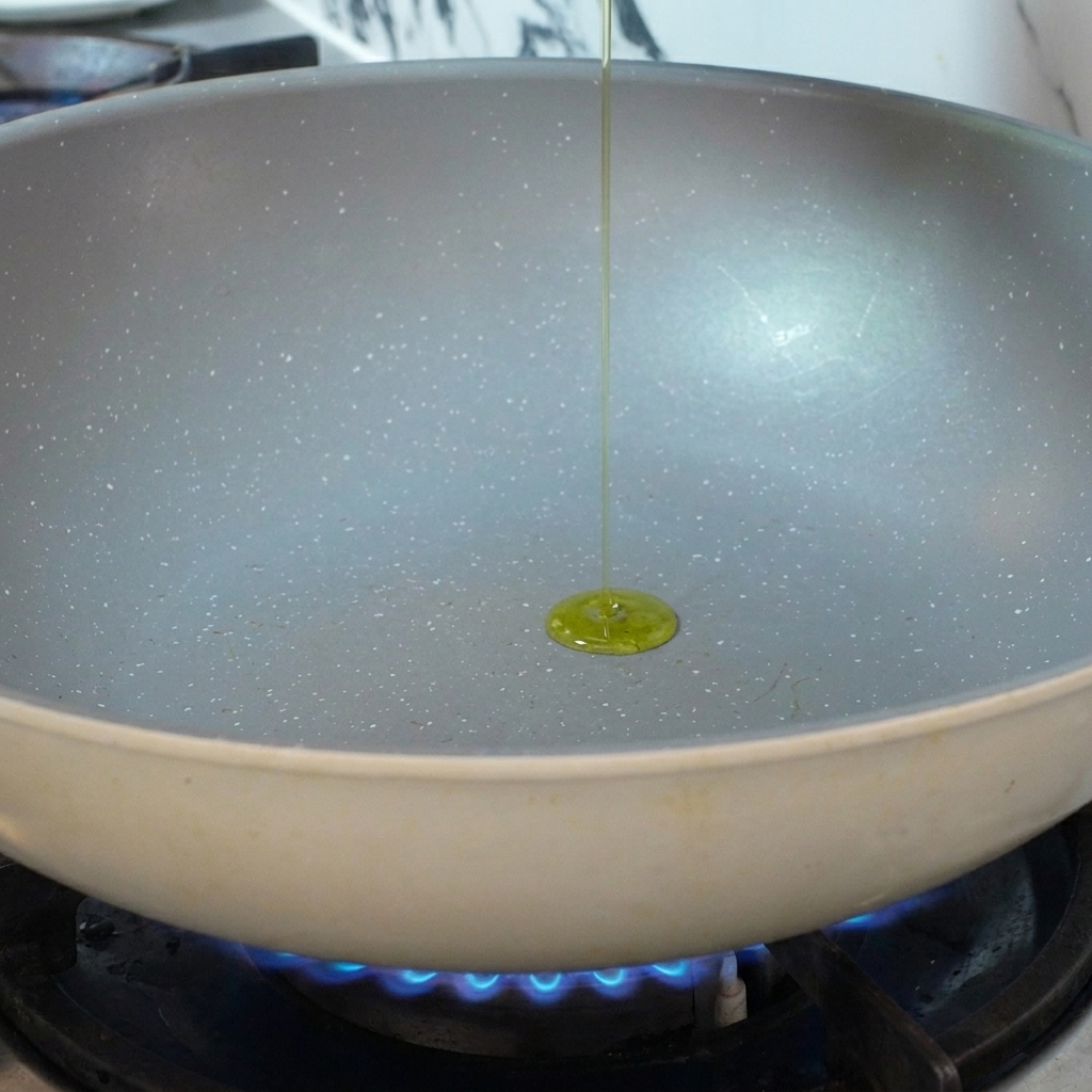 Olivenöl, das in eine vorgeheizte Keramikpfanne über einer blauen Gasflamme gegossen wird.