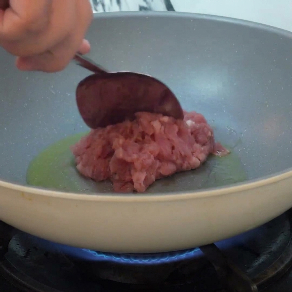 Hackfleisch, das in eine Pfanne mit heißem Öl gegeben und über einer Flamme angebraten wird.