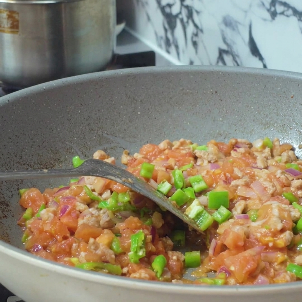 Wasser, das aus einem Behälter in eine Pfanne mit einer Mischung aus Hackfleisch und Gemüse gegossen wird.