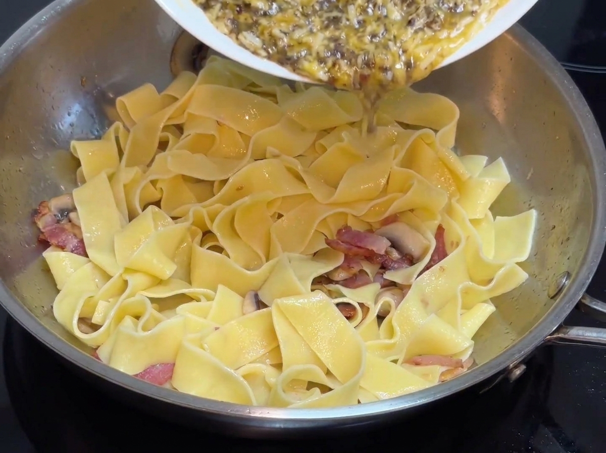 Vorbereitete schwarze Trüffelcreme-Sauce wird von einem weißen Teller in eine Edelstahlpfanne mit breiter Pasta gegossen.