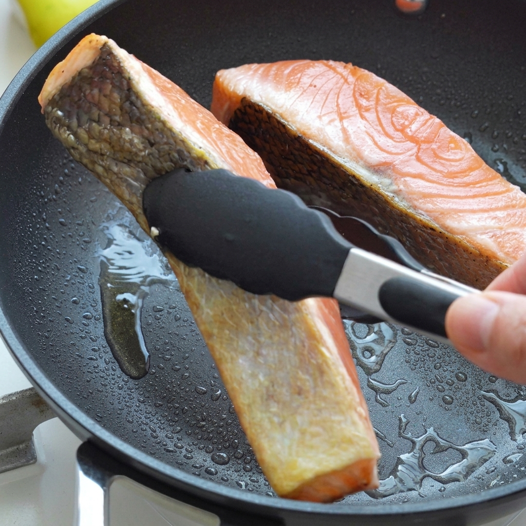 Lachsfilets werden in einer heißen Pfanne mit Öl mit einer Zange gewendet.