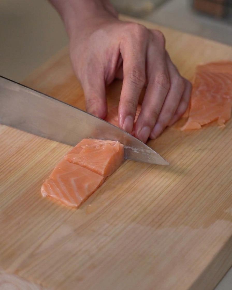 Ein frisches Lachsfilet wird auf einem Holzschneidebrett in kleine, mundgerechte Würfel portioniert.