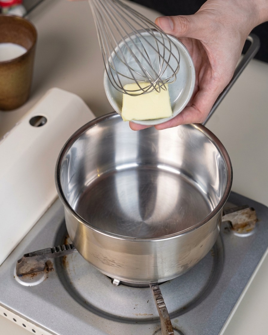 Ein kleines Stück Butter liegt in einem sauberen Metalltopf auf einem tragbaren Herd.