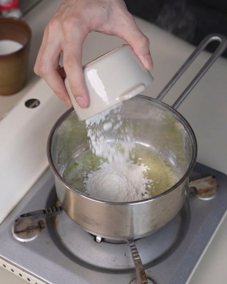 Mehl wird aus einer kleinen Schüssel zu geschmolzener Butter in einen Topf gegeben und mit einem Spatel verrührt.