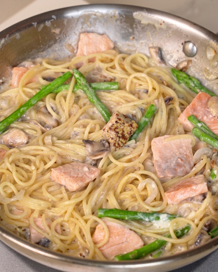 Senfsoße, Salz und Pfeffer werden in eine Pfanne mit cremiger Lachspasta eingearbeitet.