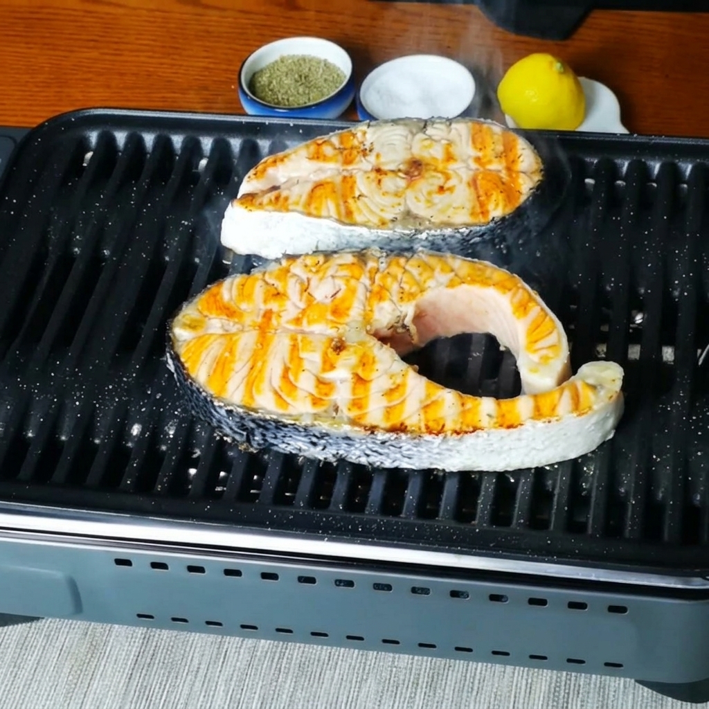 Nahaufnahme von Lachssteaks, die nach dem Würzen in der Grillpfanne brutzeln.