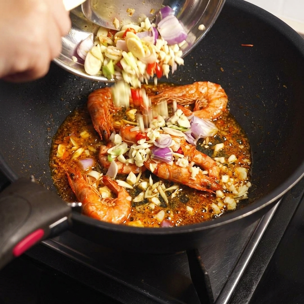Gehackte Aromaten und Tom Yum Paste werden aus einer Schüssel zu den gebratenen Garnelenschalen in die Pfanne gegeben.