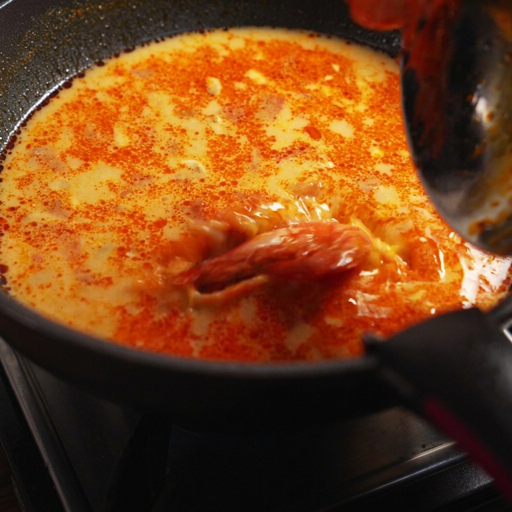 Gekochte Spaghetti, Garnelen und frischer Koriander werden in die köchelnde Sauce in der Pfanne gemischt.