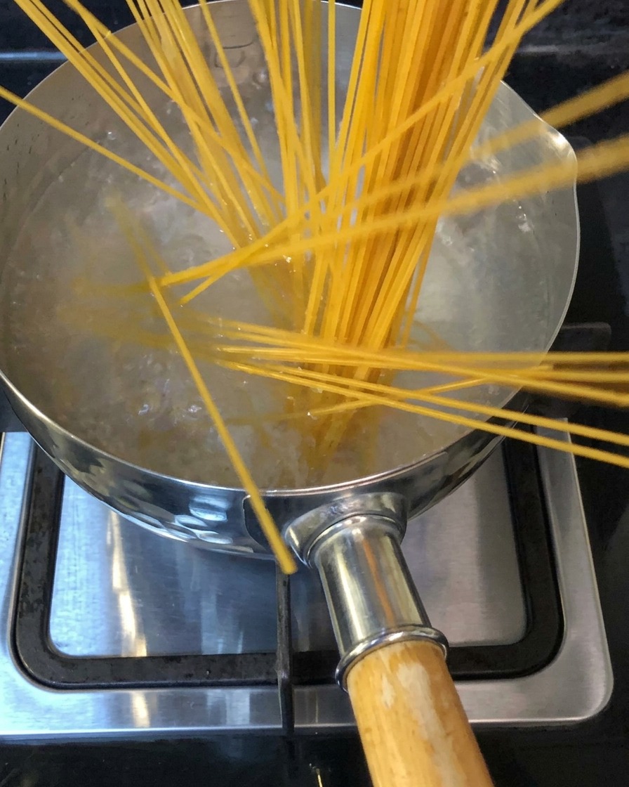 Spaghettinudeln werden in einen Topf mit kochendem Salzwasser auf einem Herd gegeben.