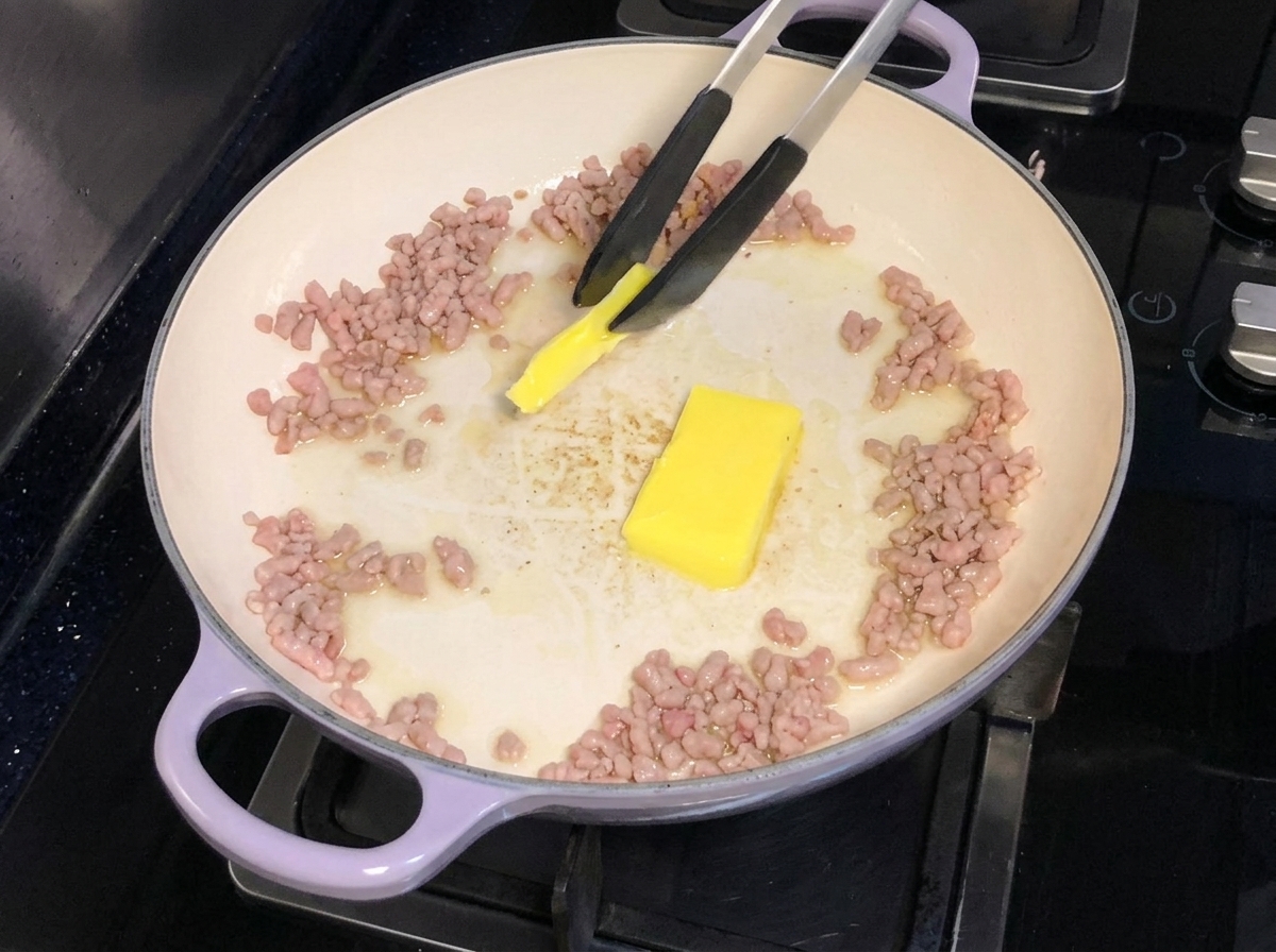Butter wird in eine Pfanne mit gebratenem Schweinehackfleisch gegeben und geschmolzen.