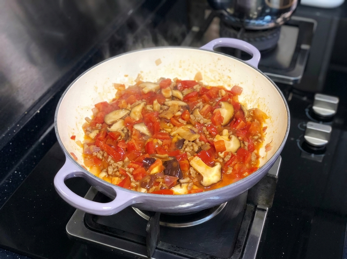 Eine lebendige Mischung aus gehackten Tomaten, Zwiebeln und Shiitake-Pilzen köchelt zusammen in einer Pfanne auf dem Herd.