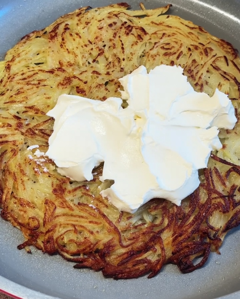 Weißer Frischkäse wird in Klecksen auf dem heißen, knusprigen Kartoffelpuffer verteilt und glattgestrichen.