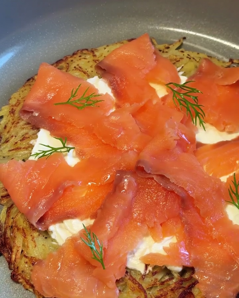 Eine fertige Kartoffel-Räucherlachs-Pizza, garniert mit frischen Dillzweigen und roten Zwiebelstückchen.