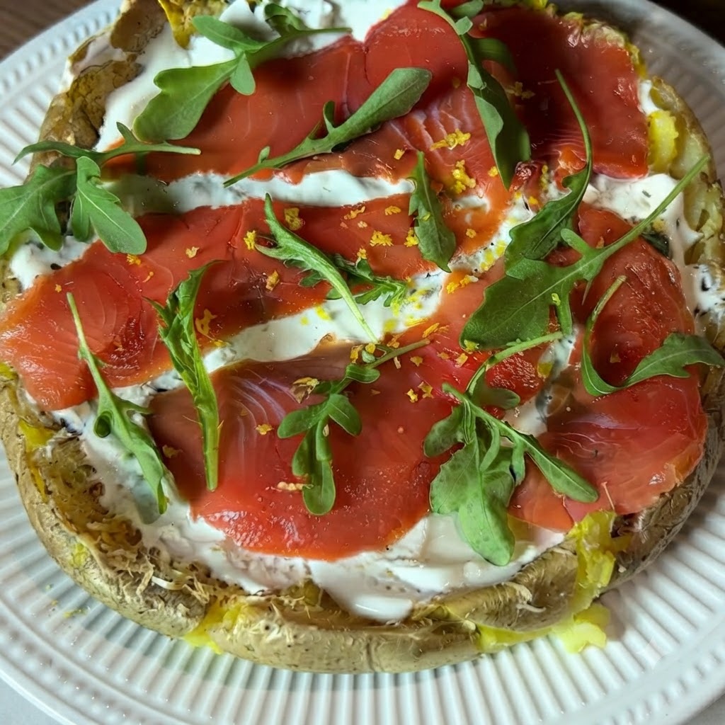 Nahaufnahme von frisch abgeriebener gelber Zitronenschale, die über die belegte Kartoffel-Pizza gestreut wird.