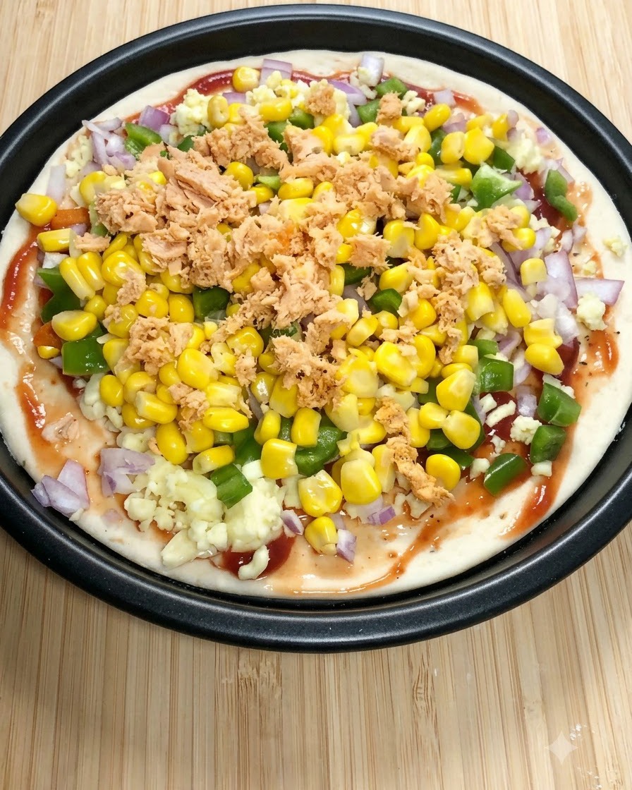 Ein runder Pizzaboden, belegt mit Tomatensoße, Mozzarella, grüner Paprika, Mais und Lachsflocken.