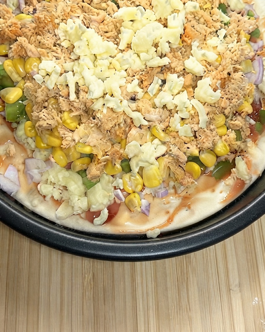 Nahaufnahme einer vorbereiteten Pizza, die üppig mit geriebenem Mozzarella bestreut wird.
