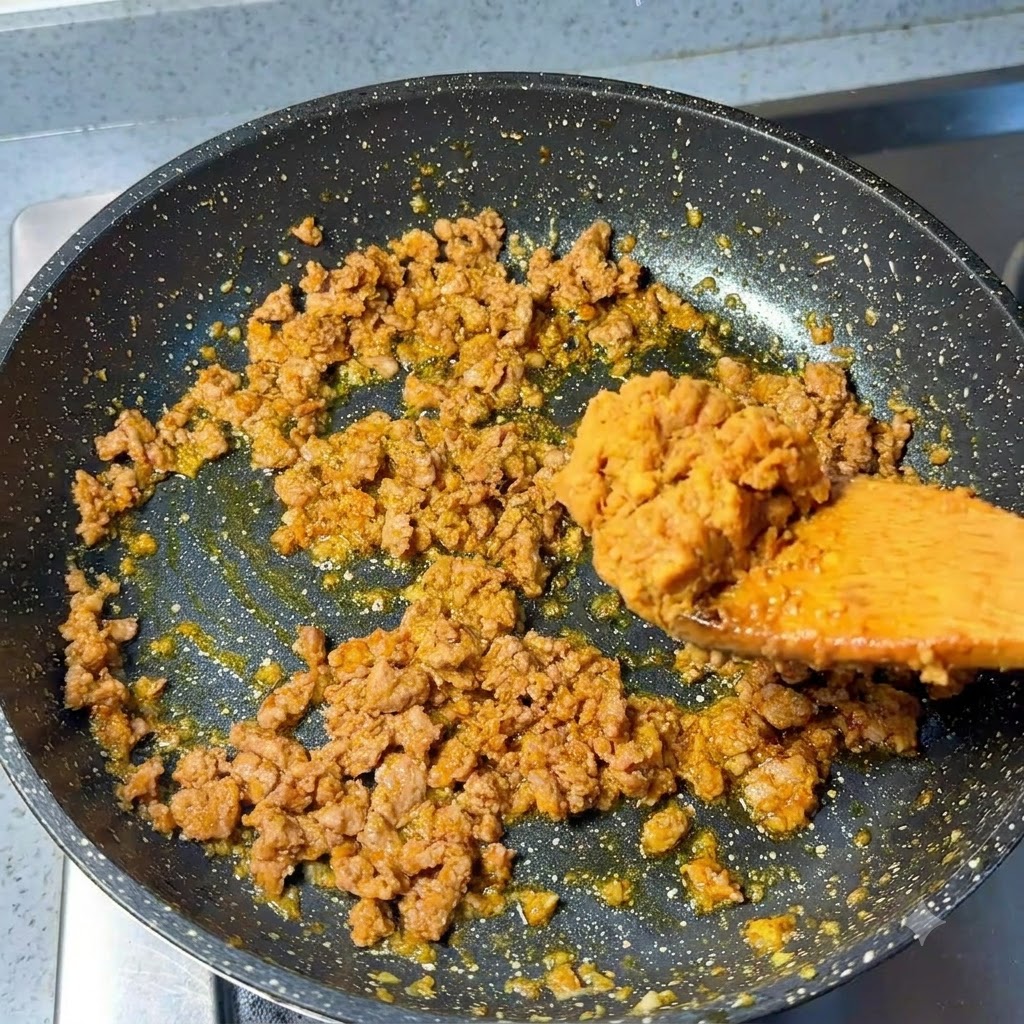 Ein Löffel Miso-Paste wird zu dem angebratenen Hackfleisch in die Pfanne gegeben.