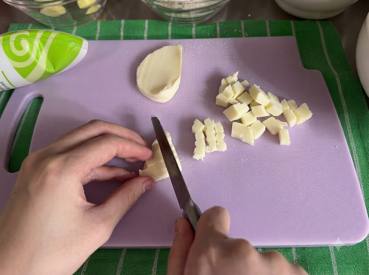 Ein Block Mozzarella-Käse wird mit einem Messer auf einem Schneidebrett in kleine Würfel geschnitten.