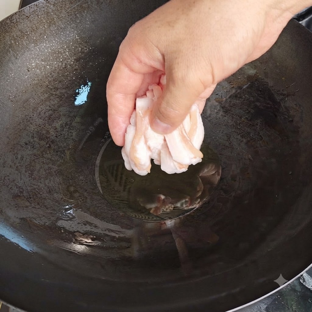 Eine Hand legt vorsichtig dünne Scheiben rohen Schweineschmalzes in einen heissen Wok mit Öl.