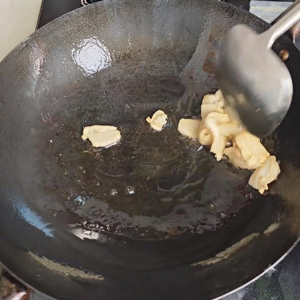 Ein Metallelöffel rührt Schweineschmalzstücke um, während sie in einem heissen Wok schmelzen.