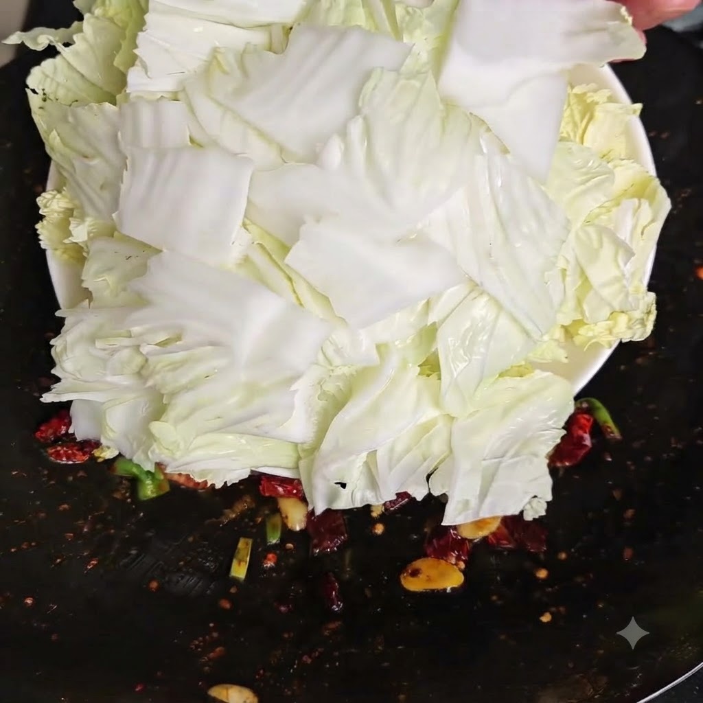 Frisch geschnittene rohe Chinakohlstücke werden von einem weissen Teller in einen heissen Wok geschüttet.