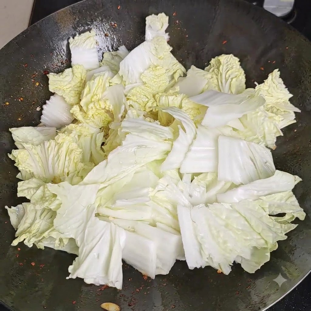 Salz wird gleichmässig über einen Berg frischer Chinakohlstücke in einem Wok gestreut.