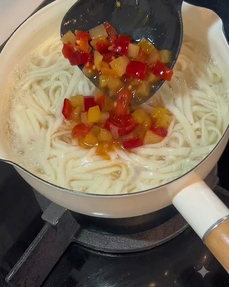 Eine Schöpfkelle gießt saure Chilisuppenbasis über einen Topf mit gekochten Nudeln.