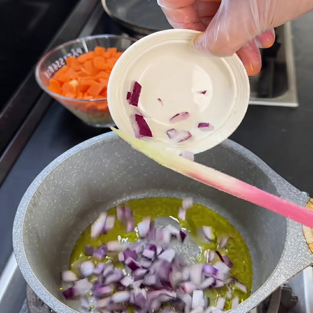 Rote Zwiebelstücke werden aus einer kleinen weißen Schüssel in einen Topf mit heißem Öl gegeben.