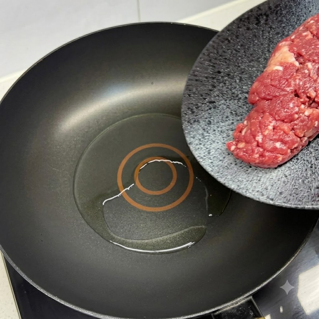Frisches Rinderhackfleisch wird in eine heiße, geölte schwarze Pfanne mit einem roten Pfannenwender gegeben.