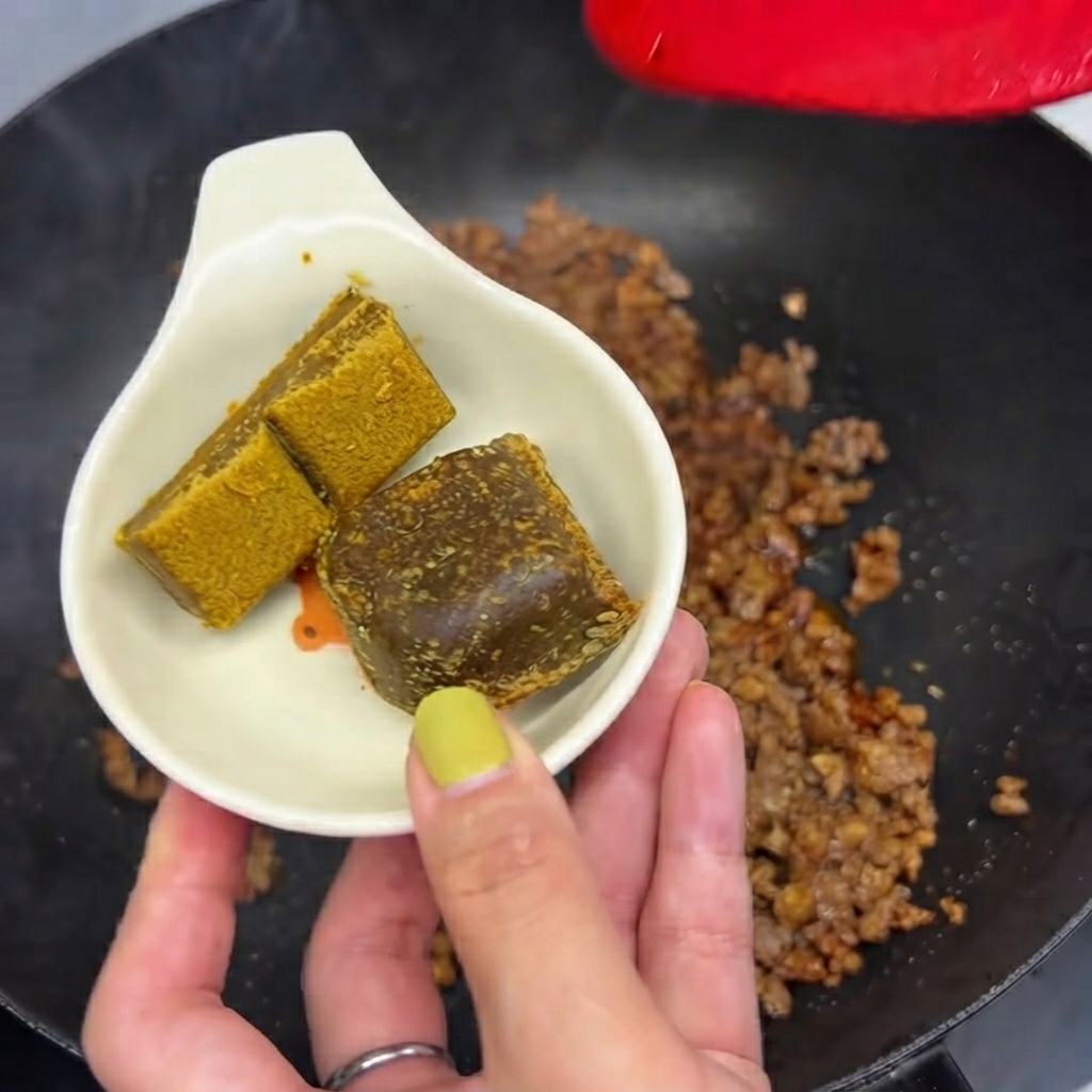 Zwei Curryblöcke in einer kleinen weißen Schale bereit, um in die Pfanne mit dem Hackfleisch gegeben zu werden.