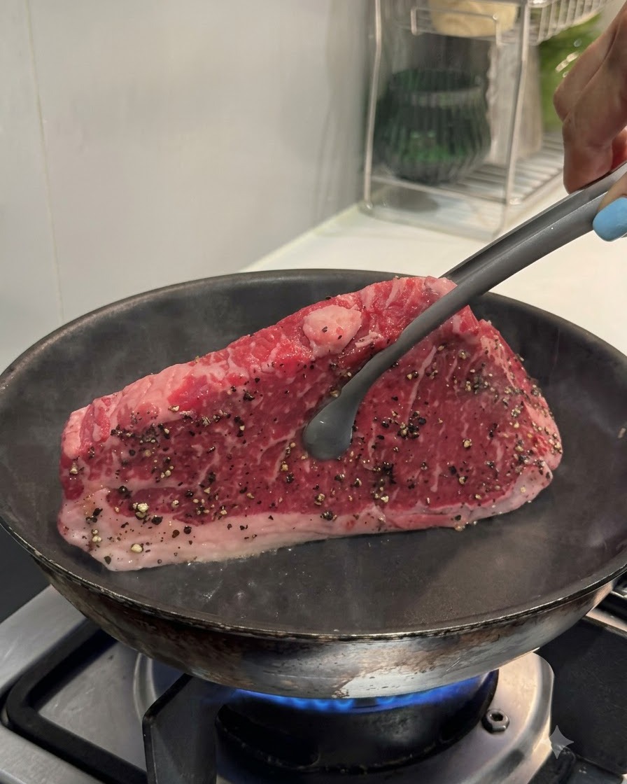 Eine Zange hält ein Steak aufrecht in einer heißen Pan, um die Kante anzubraten.
