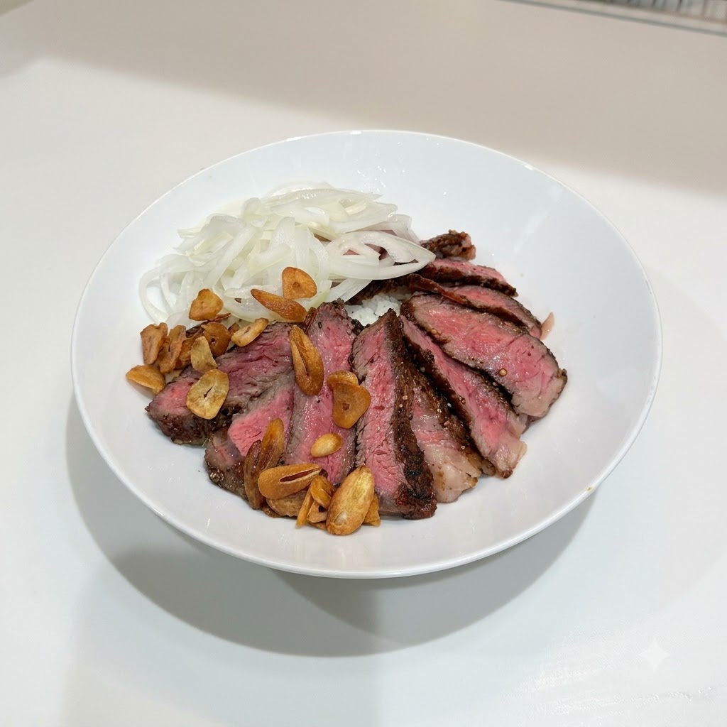 Eine weiße Schüssel mit Steak, Zwiebeln und goldenen Knoblauchchips auf Reis.