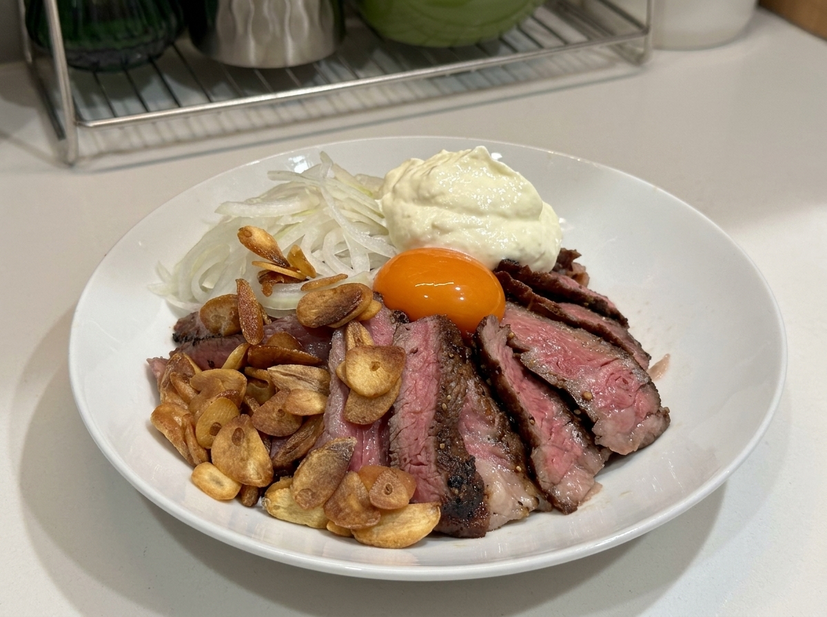 Eine Schüssel mit Steak, Knoblauchchips, Zwiebeln, Eigelb und einer großen Portion Schlagsahne oben drauf.