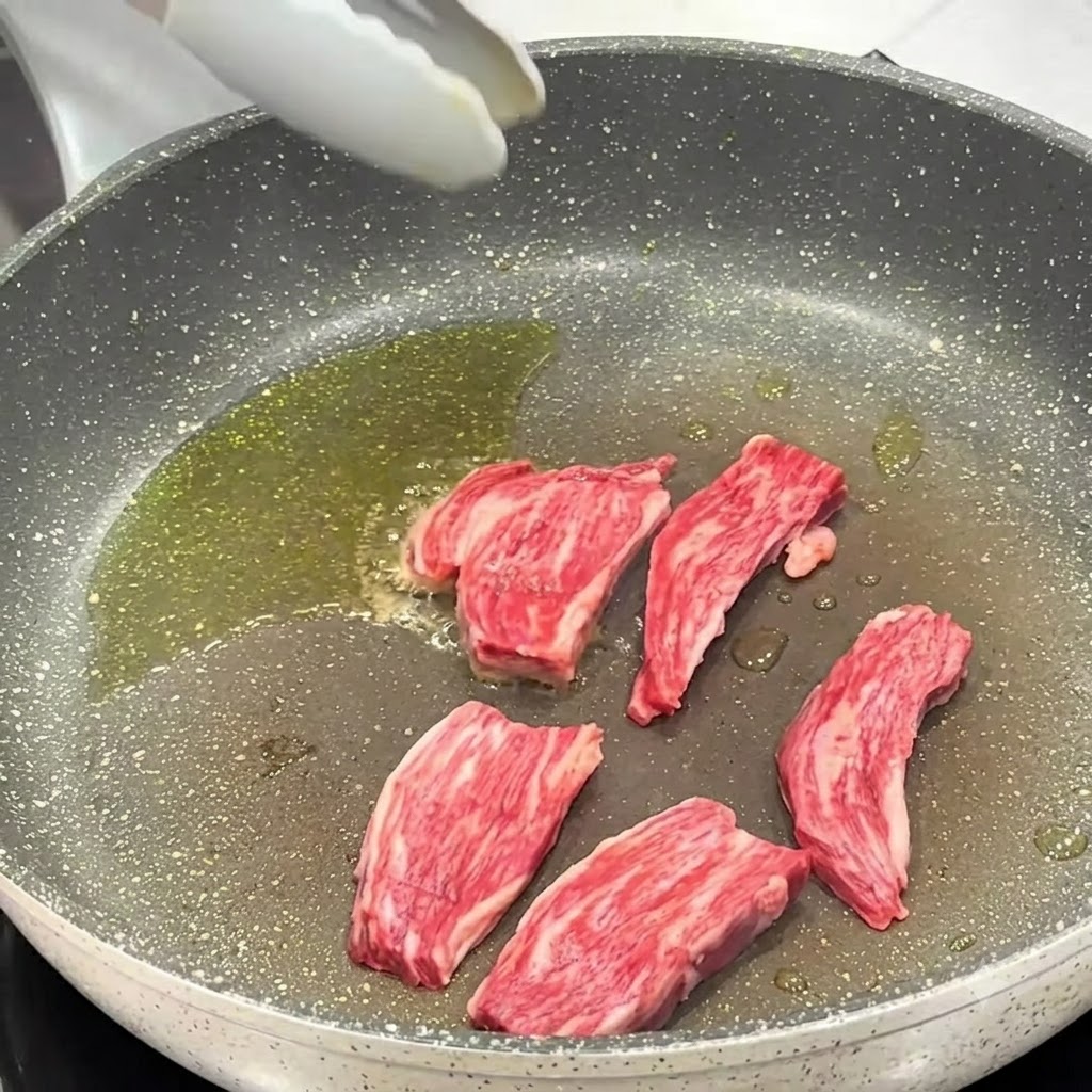 Salz und schwarzer Pfeffer werden auf die in der Pfanne garen Steakstücke gestreut.