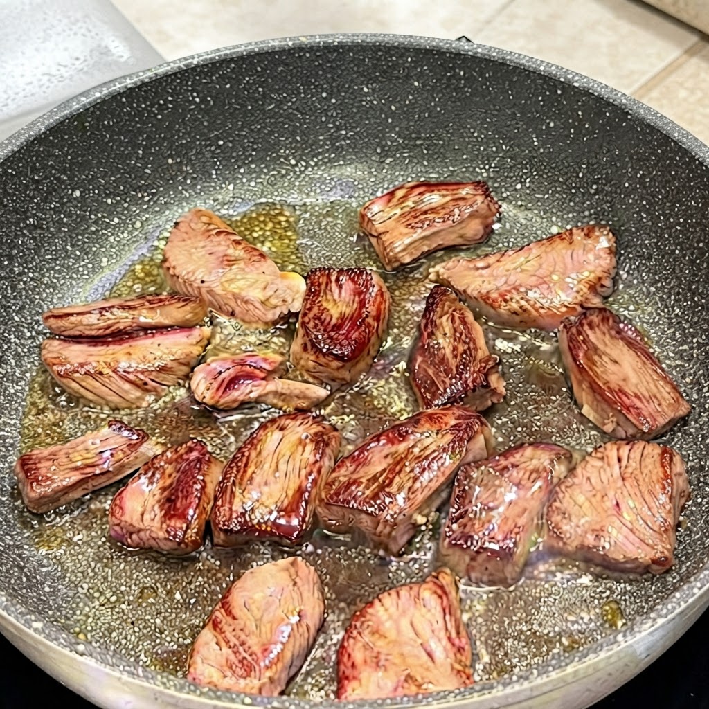 Eine Zange wendet Flanksteakstücke in einer Pfanne, um gebräunte Oberflächen zu zeigen.