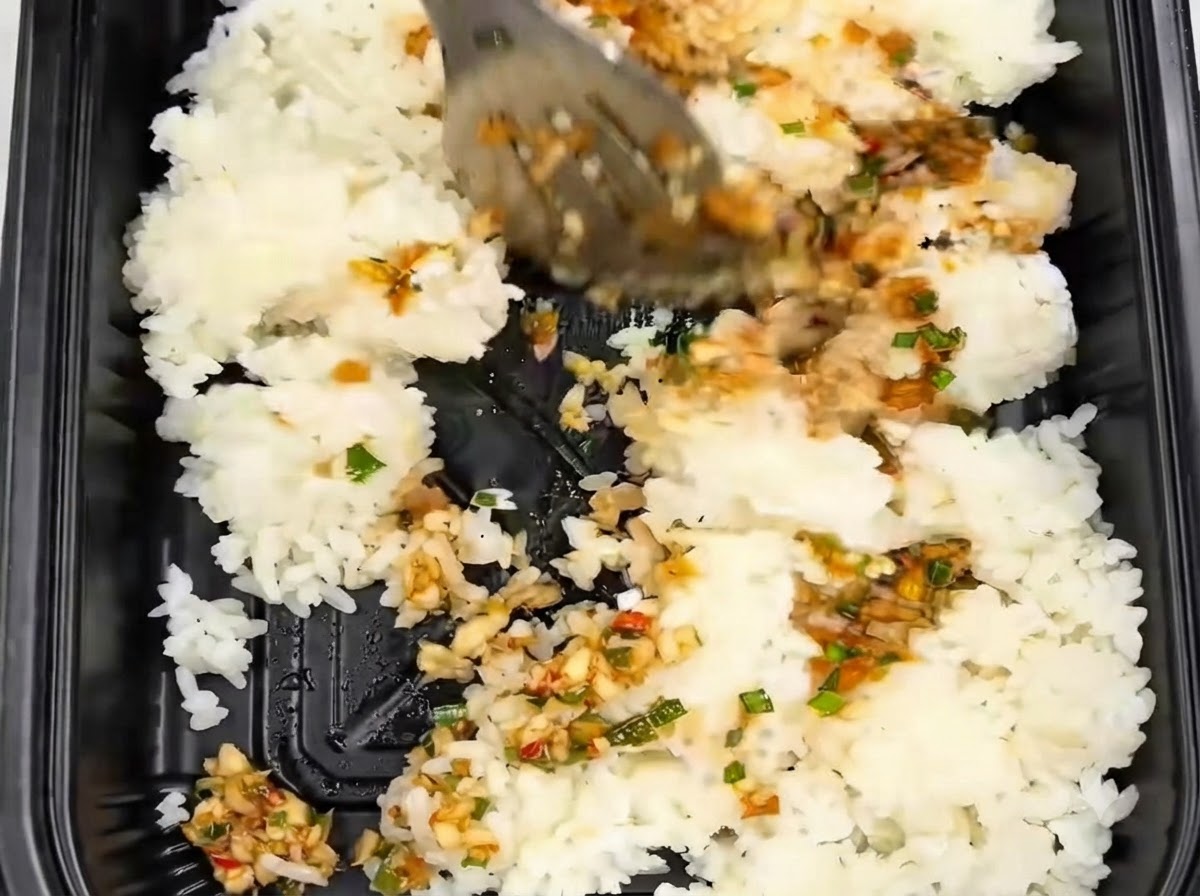 Reis wird mit einer Zange in einem schwarzen Behälter neben Knoblauchsauce umgerührt und gemischt.
