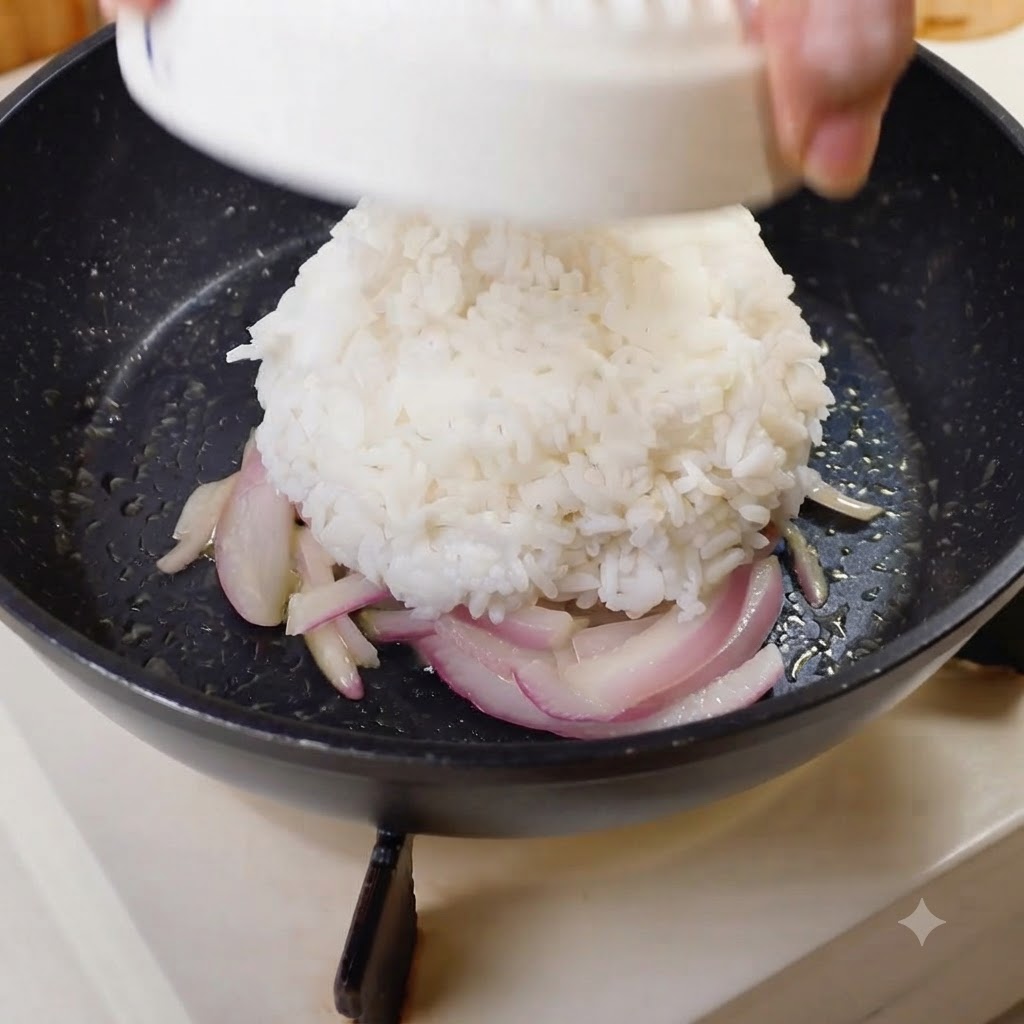 Eine kuppelförmige Portion weißer Reis wird in die Mitte der Pfanne auf die Zwiebeln gestürzt.