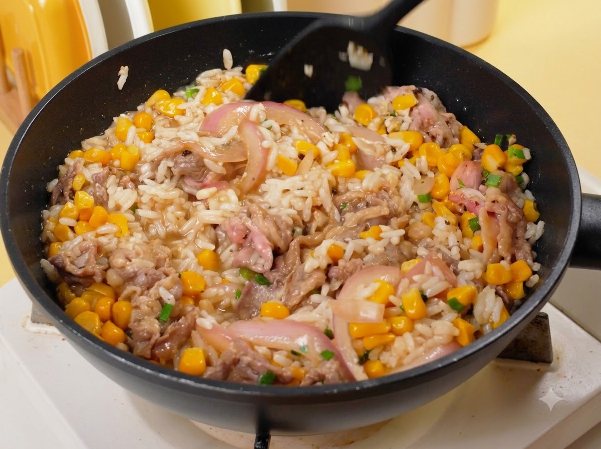 Ein schwarzer Pfannenwender mischt Reis, Rindfleisch, Mais und Zwiebeln in der Pfanne.