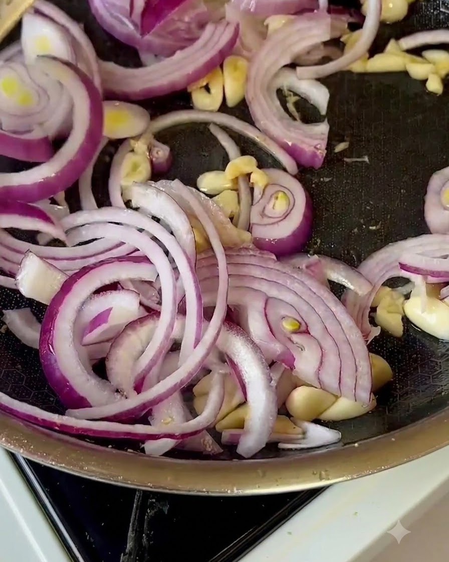 Geschnittene rote Zwiebeln, Knoblauch und Apfelstücke werden in einer Bratpfanne durchgeschwenkt.