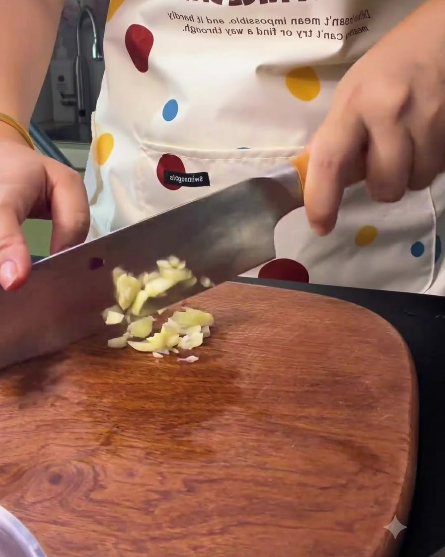 Knoblauchzehen werden mit einem Küchenmesser auf einem Holzbrett zerkleinert und gehackt.