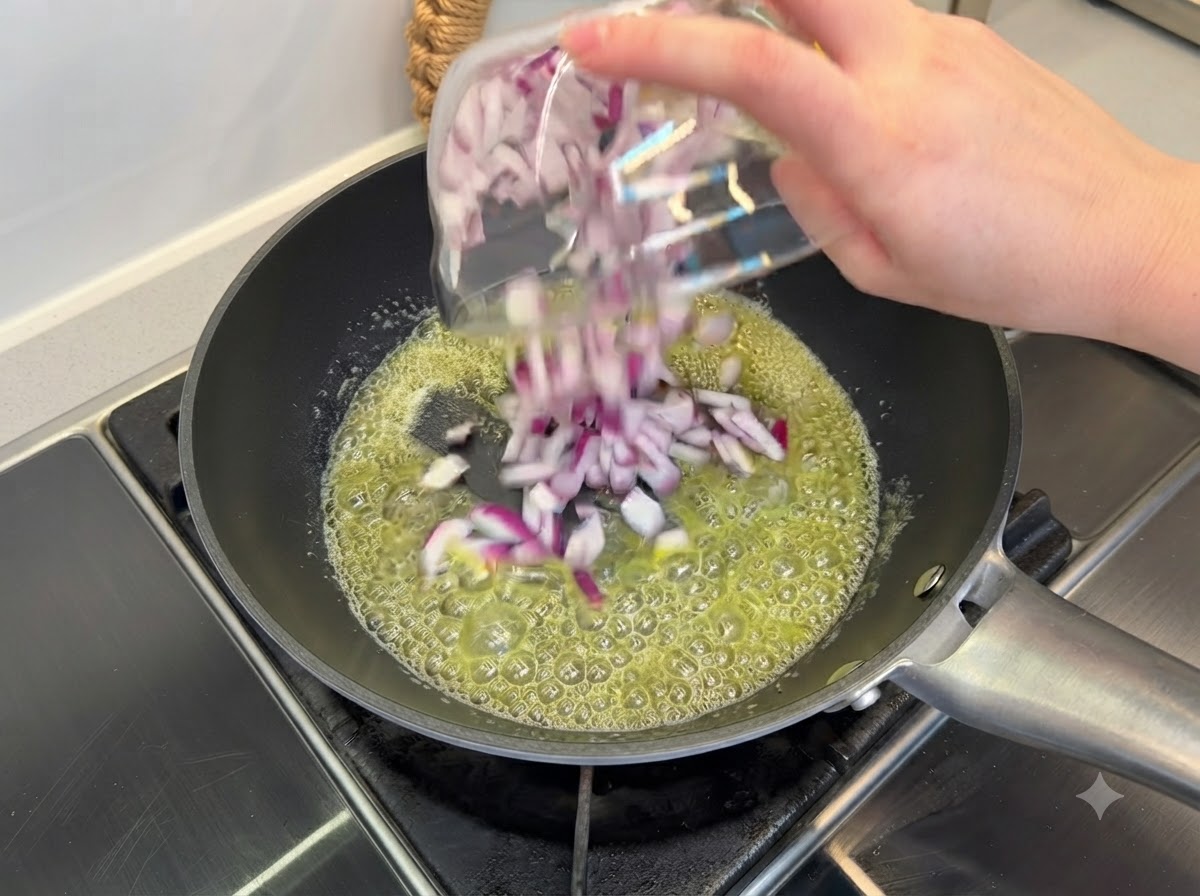 Gewürfelte rote Zwiebeln werden in zerlassener Butter in einer schwarzen Bratpfanne angebraten.