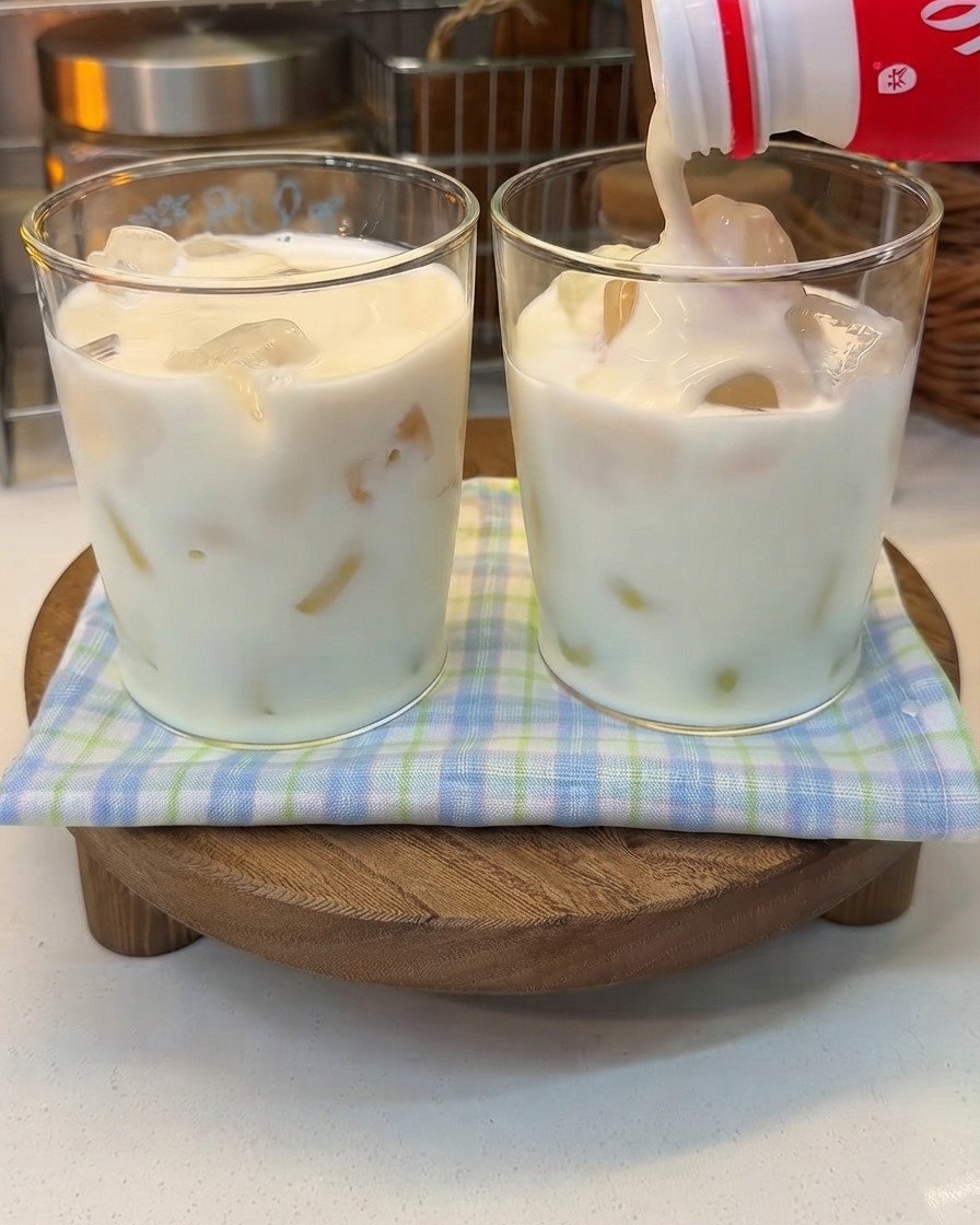 Dicker Joghurt wird aus einer Flasche in ein Glas mit eisgekühlter Milch gegossen.