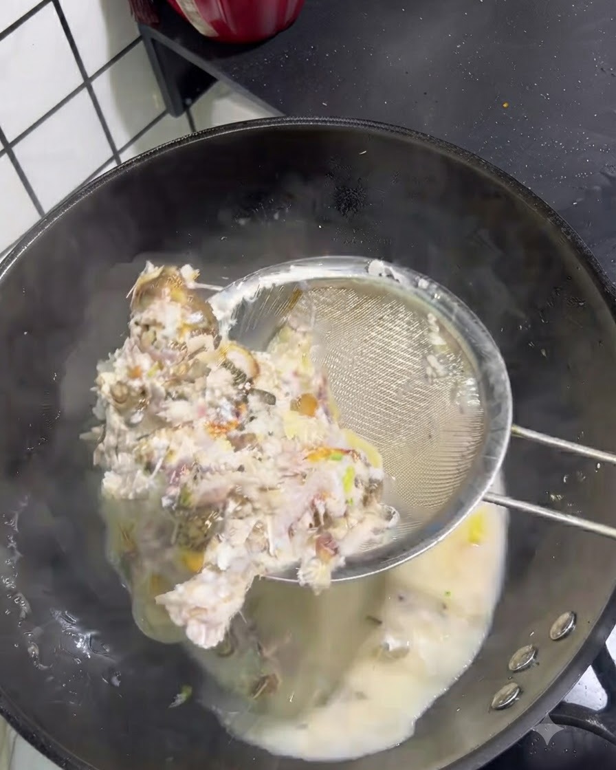 Feste Fischgräten und Fleisch werden mit einem Drahtsieb aus einer milchigen Brühe geschöpft.