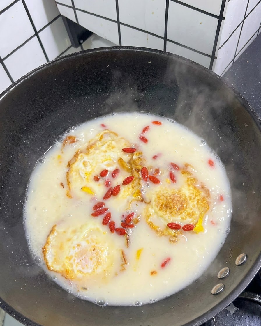 Getrocknete rote Gojibeeren verstreut auf der Oberfläche einer köchelnden weißen Suppe mit Spiegeleiern.