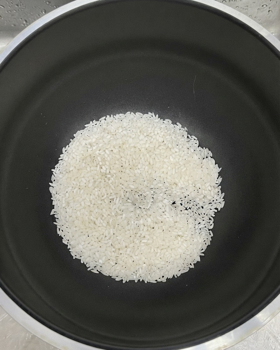 Weißer Reis am Boden eines schwarzen Topfes mit hinzugefügtem Wasser zum Spülen.